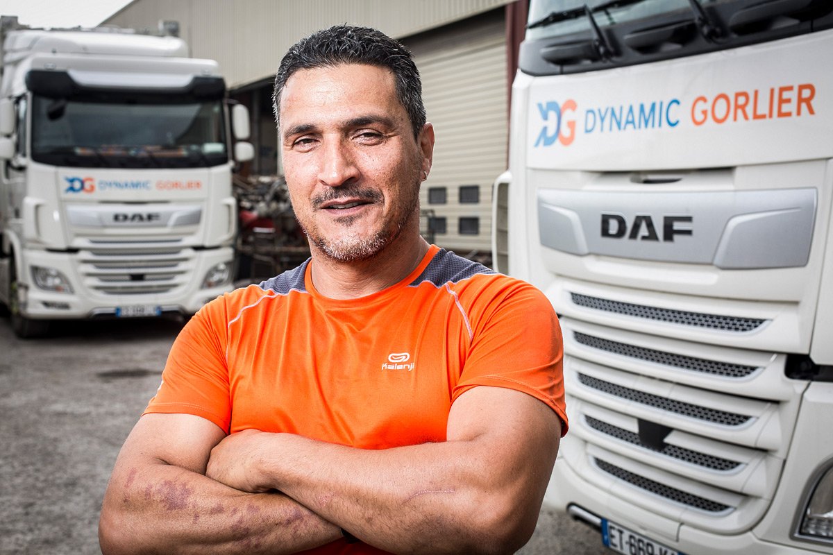 Portrait d'un chauffeur routier devant les camions de la société Dynamic Gorlier